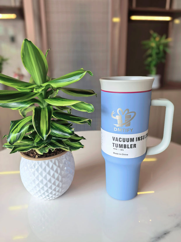Blue vacuum insulated tumbler on a table with a plant in the background