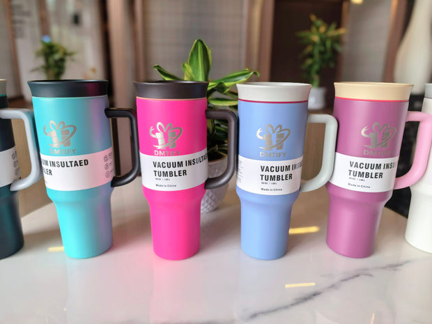 Set of colorful vacuum insulated tumblers on a marble surface with plants in the background.