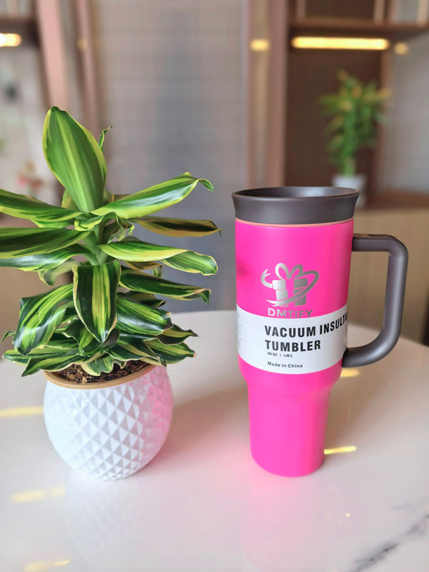 Pink vacuum insulated tumbler with black lid on a surface next to a potted plant.
