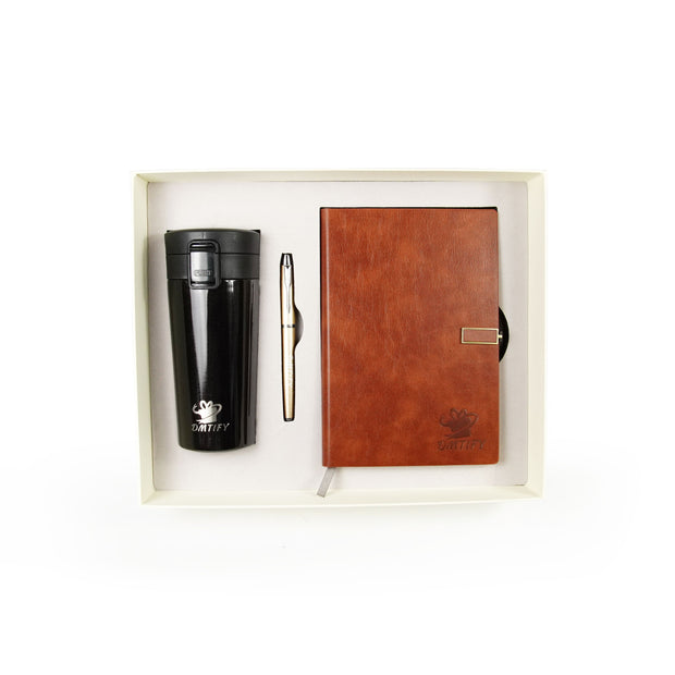 Set of black travel mug, brown notebook, and pen in a box on a white background