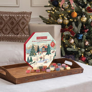 Fragrance advent calendar with candles on a wooden tray in front of a decorated Christmas tree.