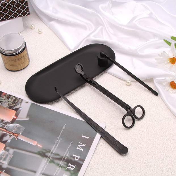 Black Set of candle accessories including wick trimmer, dipper, snuffer and tray with a magazine and small container in the background