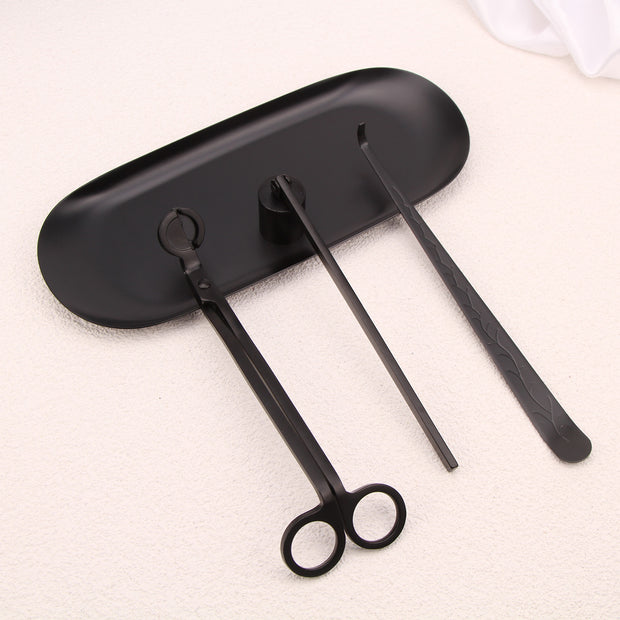 Set of black candle accessories including wick trimmer, dipper, snuffer and tray on a white surface.