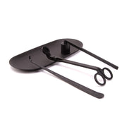 Black candle care tools Set including wick trimmer, dipper, snuffer and tray on a white surface with decorative items on a white background