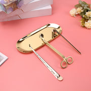 Gold candle care tools on a pink background with flowers and books.