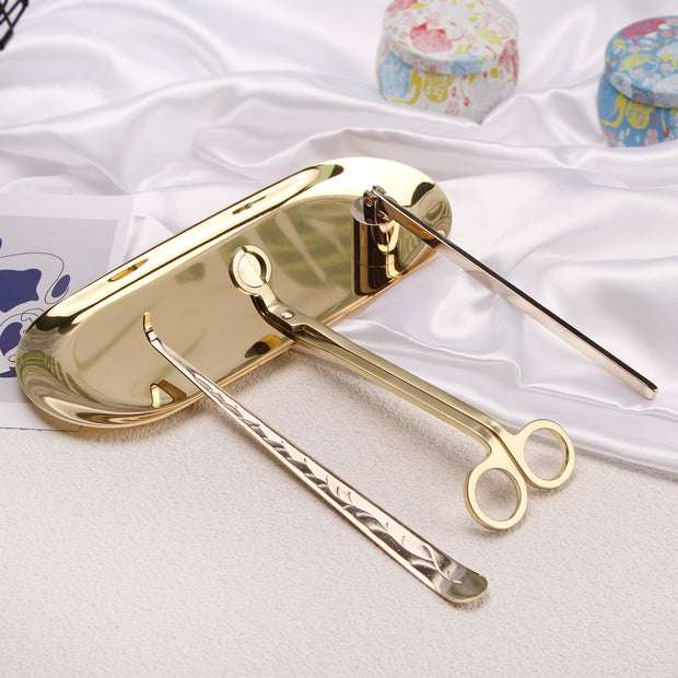 Gold Set of candle accessories including wick trimmer, dipper, snuffer and tray on a white surface.