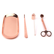 Set of rose gold candle accessories including wick trimmer, dipper, snuffer and tray on a white surface.