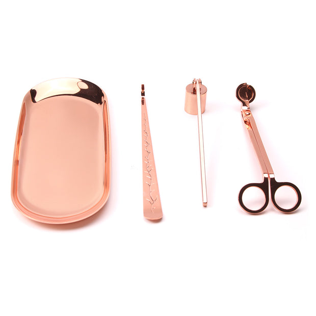 Set of rose gold candle accessories including wick trimmer, dipper, snuffer and tray on a white surface.